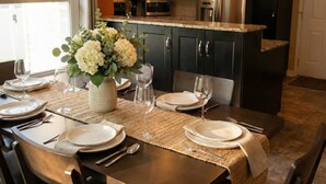 Un coin repas avec une table dressée pour quatre personnes, un vase de fleurs et, en arrière-plan, des appareils de cuisine modernes.