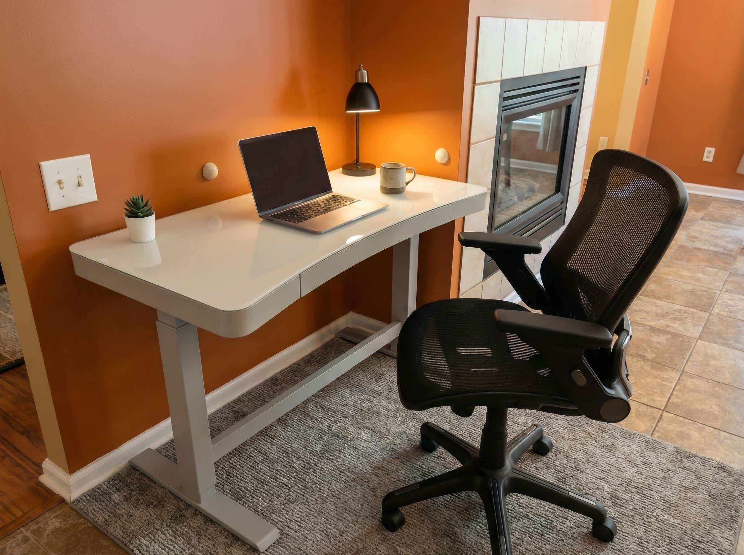 A modern office space with a white desk, a laptop, a black office chair, a small potted plant, a lamp, and a window with blinds.