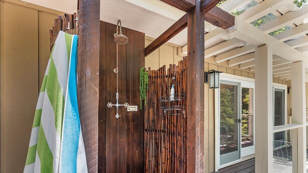 A wooden shower enclosure with a rain showerhead, a towel rack with a striped towel, and a wooden fence with hanging plants.