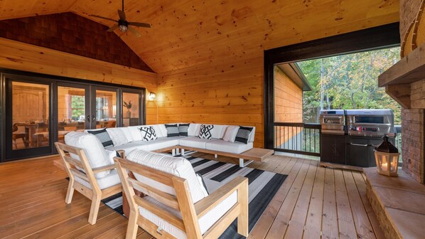 A wooden deck with a sectional sofa, a dining area, and a barbecue grill.