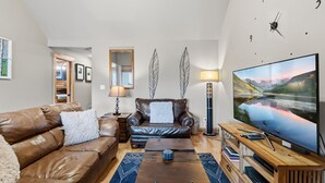 Ein modernes Wohnzimmer mit einem Ledersofa, einem Holztisch und einem großen Flachbildfernseher.