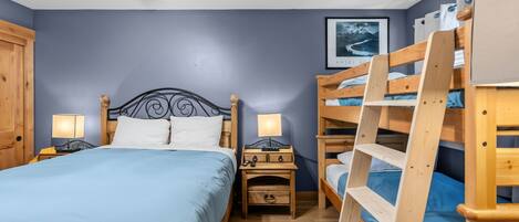 Un dormitorio con una cama individual, una mesita de noche, un aparador y una cama litera.