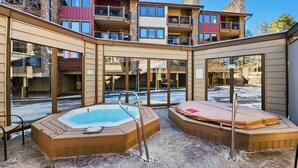 Ein Poolbereich mit Whirlpool, Holzterrasse und Blick auf ein mehrgeschossiges Gebäude mit Balkonen.