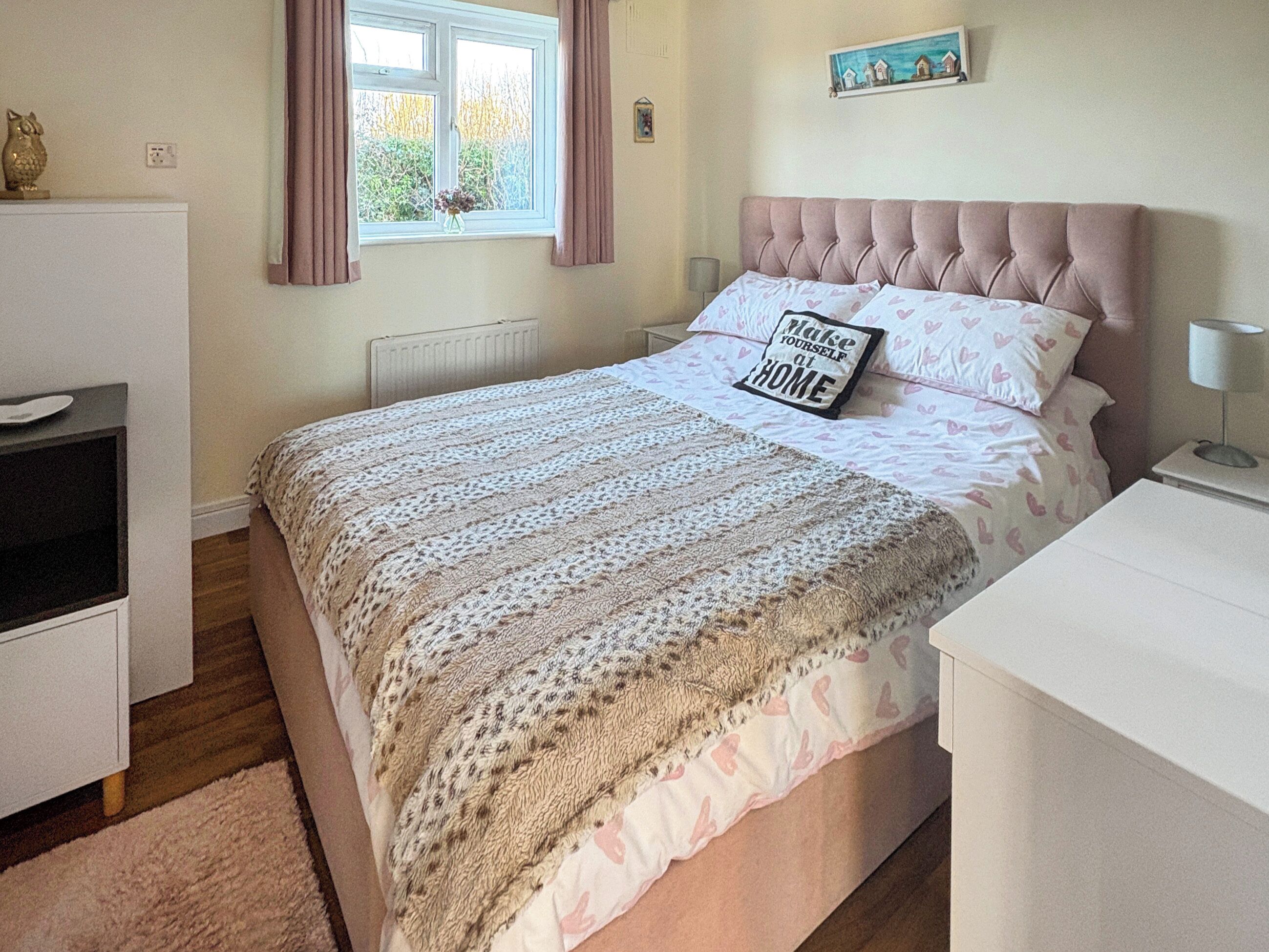 Un dormitorio ordenado con cama, mesitas de noche, cómoda y ventana con cortinas.