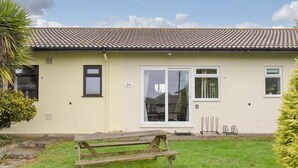 A single-story building with a tiled roof, numbered 24 and 25, a front door with glass panels, and a small garden area with a wooden bench. - Barn Owls Holiday Bungalow (Weston, near Sidmouth)