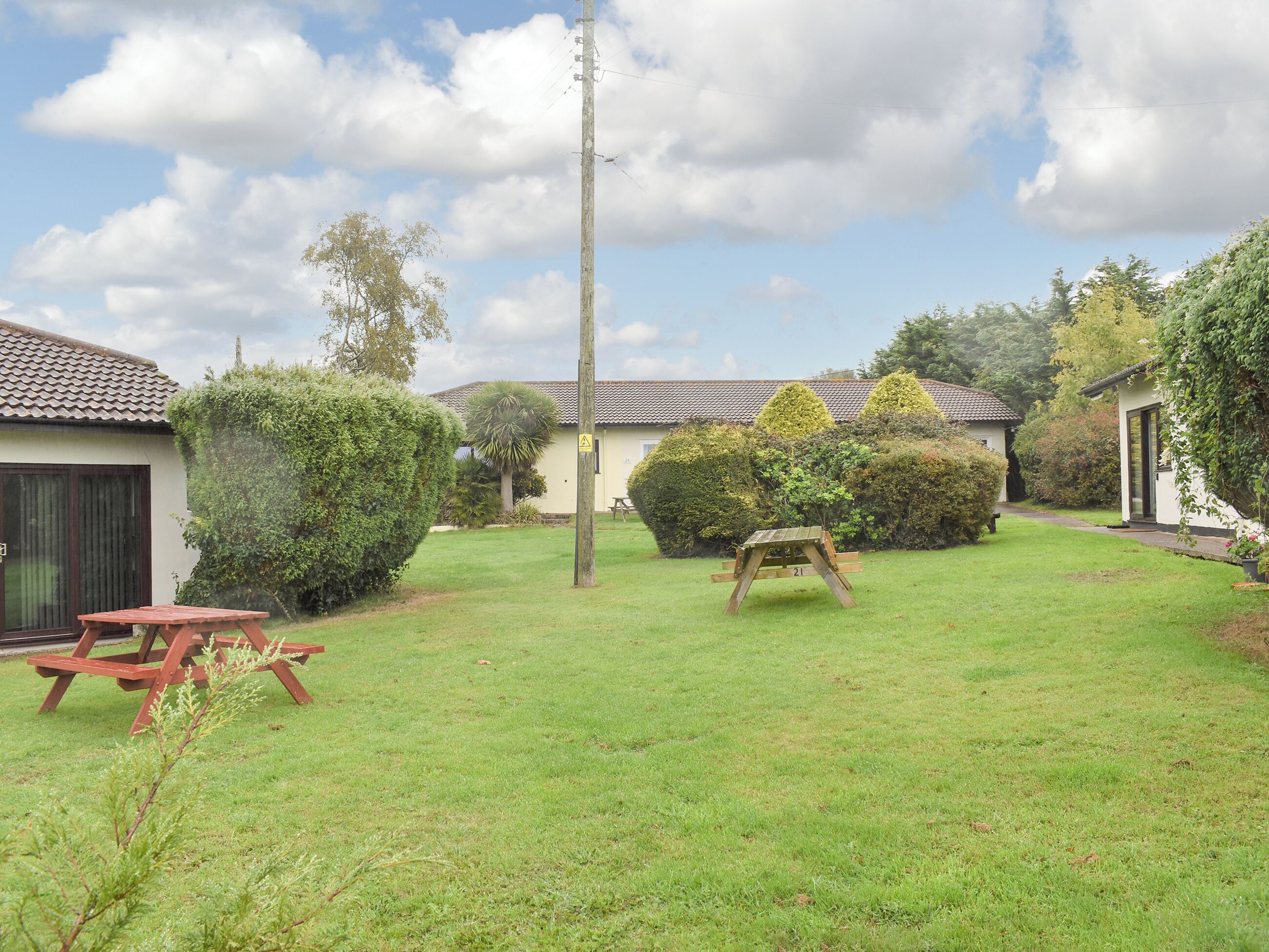 A well-maintained garden with a picnic table and a wooden bench, surrounded by neatly trimmed hedges and a building with a tiled roof.