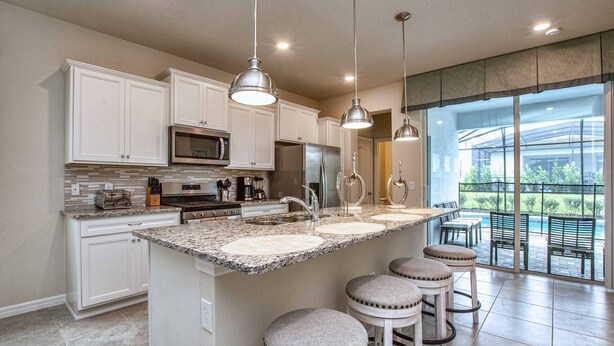 Una cocina moderna con armarios blancos, encimeras de granito, electrodomésticos de acero inoxidable y una isla grande con taburetes de bar.