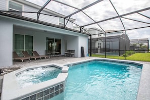 A swimming pool with a hot tub, surrounded by a covered patio with lounge chairs.