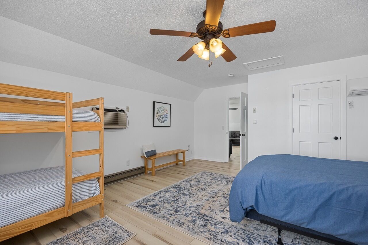 Una habitación con literas, ventilador de techo, banco y una puerta.