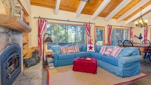 Ein gemütliches Wohnzimmer mit Kamin aus Stein, einem blauen Ecksofa und einem roten Hocker.