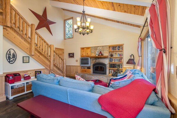 A cozy living room with a wooden staircase, a fireplace, a bookshelf, and a large star decoration. - Candy's Cottage- Perfect ski weekend getaway! (Camp Connell)