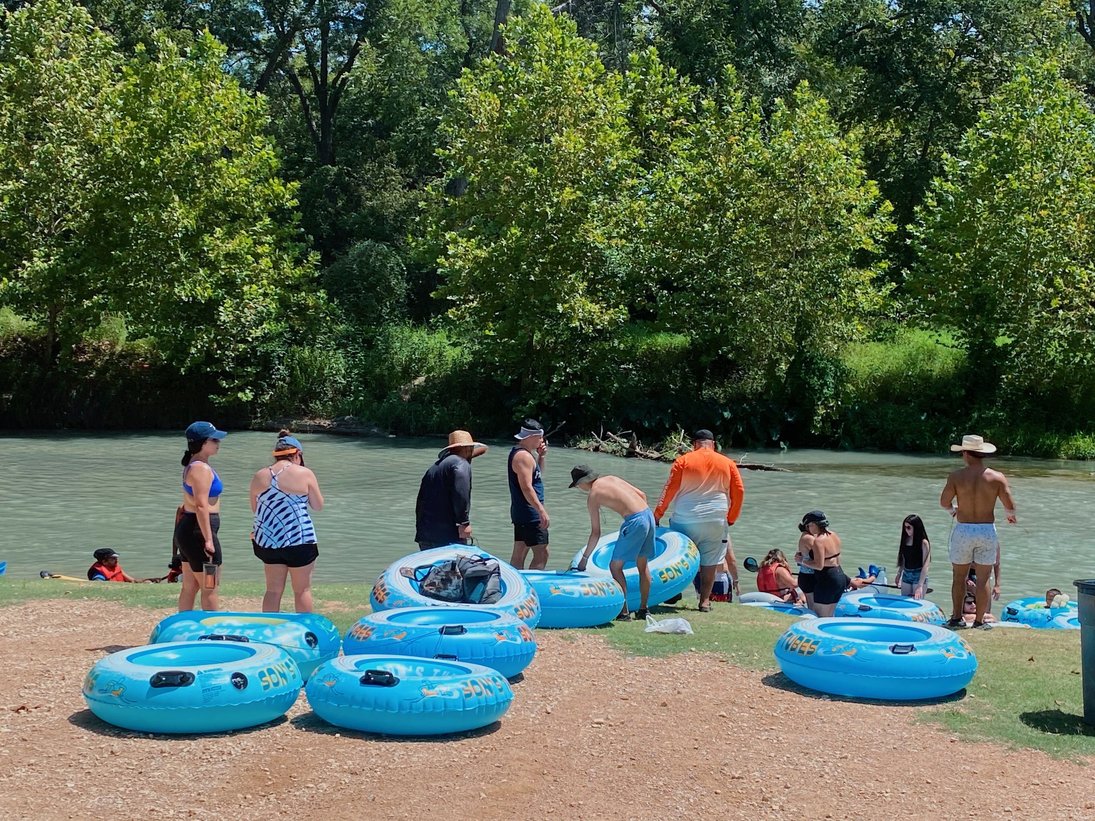 A group of people near a river with inflatable tubes and a boat.