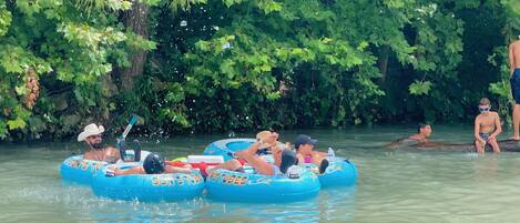 People floating on blue inflatable tubes in a body of water surrounded by dense green foliage.