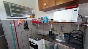 A kitchen with a stove, sink, and microwave. There are cleaning tools hanging on the wall, and a window above the stove. - Lar Recife Olinda Praia 2 (Recife)