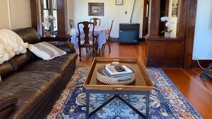 A living room with a leather sofa, a coffee table with books, a patterned rug, and a dining area with a table and chairs.