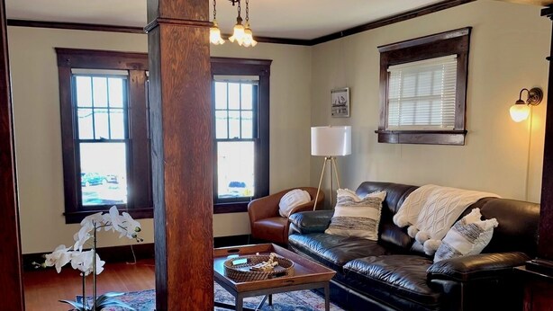 A spacious living room with a wooden floor, a leather sofa, a coffee table, and a large window with blinds.