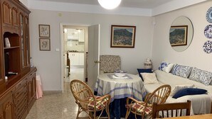 A living room with a dining table, two wicker chairs, a sofa, and a kitchen in the background. - Well equipped apartment with easy parking. Ideal starting point for your routes. (Trujillo)