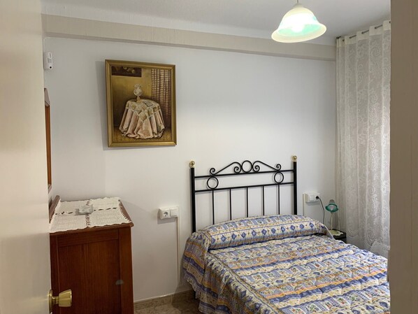 Een slaapkamer met een bed, een houten dressoir, een wandlamp en een ingelijst kunstwerk.