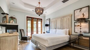 A bedroom with a large bed, a fireplace, a chair, and a nightstand with a lamp.