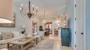 A spacious living room with a large sofa, a wooden coffee table, and a chandelier. There is a dining area with a table and chairs in the background.