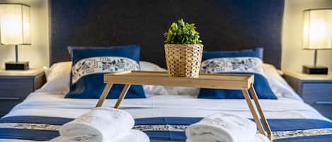 A neatly made bed with blue and white bedding, a small woven plant on a wooden tray, and two bedside lamps.