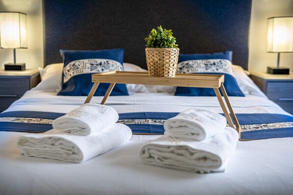 A neatly made bed with blue and white bedding, a small woven plant on a wooden tray, and two bedside lamps.