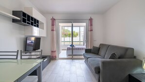 Un salon moderne avec un canapé, une table en verre, un téléviseur et un balcon agrémenté de rideaux.