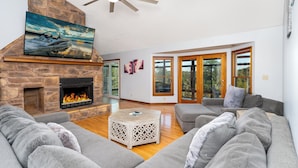A spacious living room with a stone fireplace, grey sofas, and a ceiling fan. - 6 Bedroom home, heated private pool, person Hot tub, Waterfront Views, and more (Monticello)