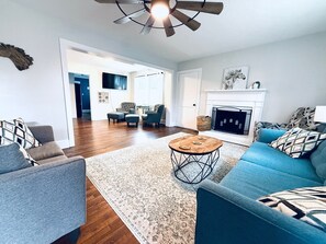 Un salon spacieux doté de planchers en bois franc, d’un canapé bleu, d’une table basse et d’une cheminée.
