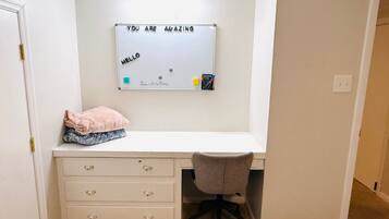 A small, neatly organized room with a white desk, a chair, and a whiteboard above the desk.