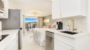 A modern hotel room with a kitchen area, a bed with a view, and a large window. - 37th FLR Elegant Ocean View Studio|King Bed|Waikiki (Honolulu)