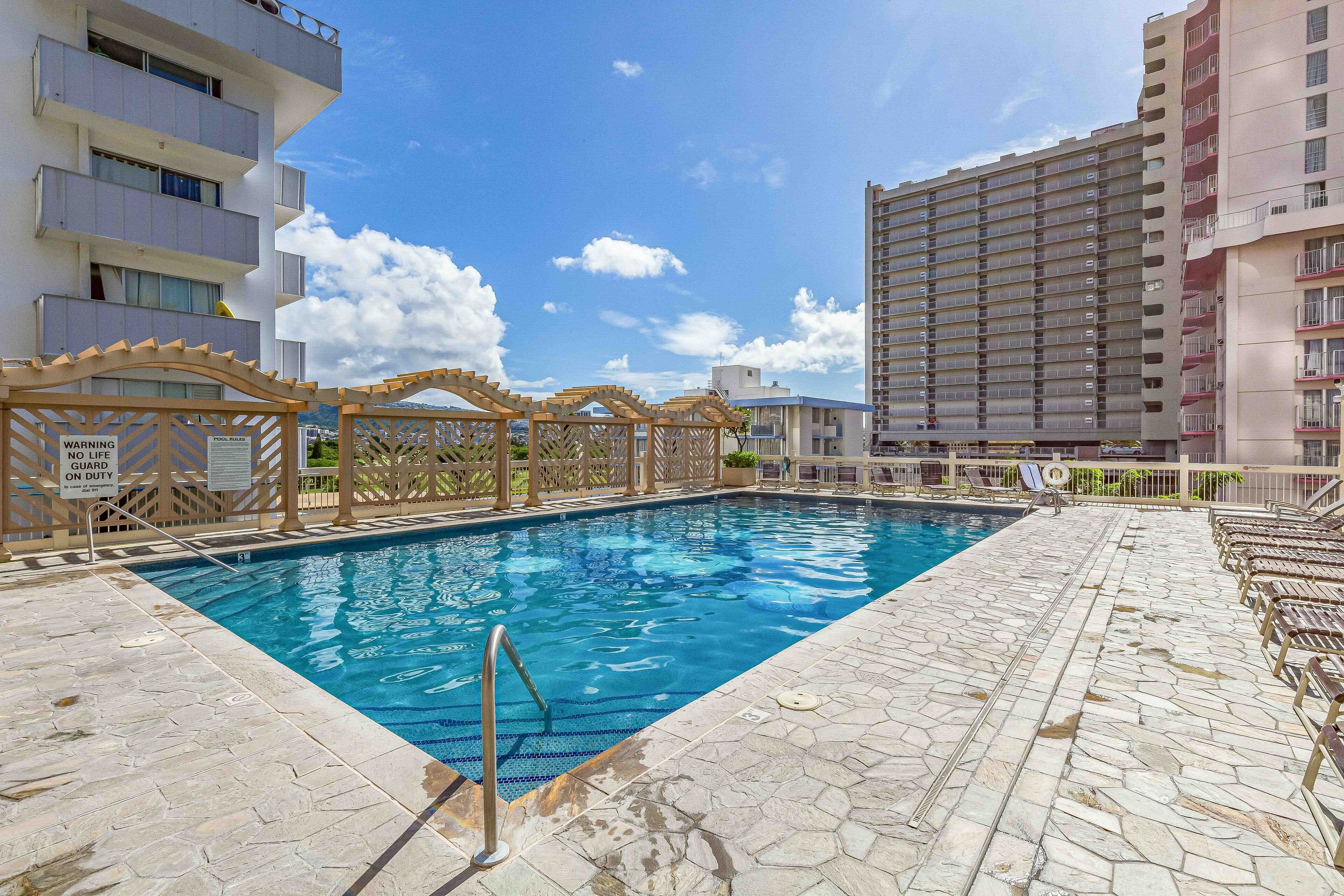 A swimming pool with a wooden deck and a lifeguard stand, surrounded by high-rise buildings.