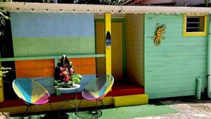 A colorful outdoor seating area with two chairs and a table, a small step leading to a door, and a decorative seahorse on the wall. - Studio Cosy, Maisonnette Créole, 100m Jolie Plage (Pointe-à-Pitre)