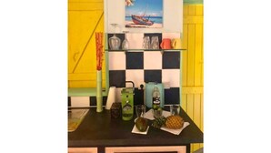 A kitchen with a checkered backsplash, a painting of a boat on the wall, and various kitchen items on the counter. - Studio Cosy, Maisonnette Créole, 100m Jolie Plage (Pointe-à-Pitre)