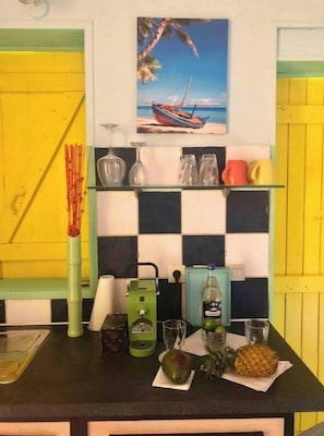 Une cuisine avec un dosseret à carreaux, un tableau représentant un bateau accroché au mur et divers ustensiles de cuisine disposés sur le plan de travail.