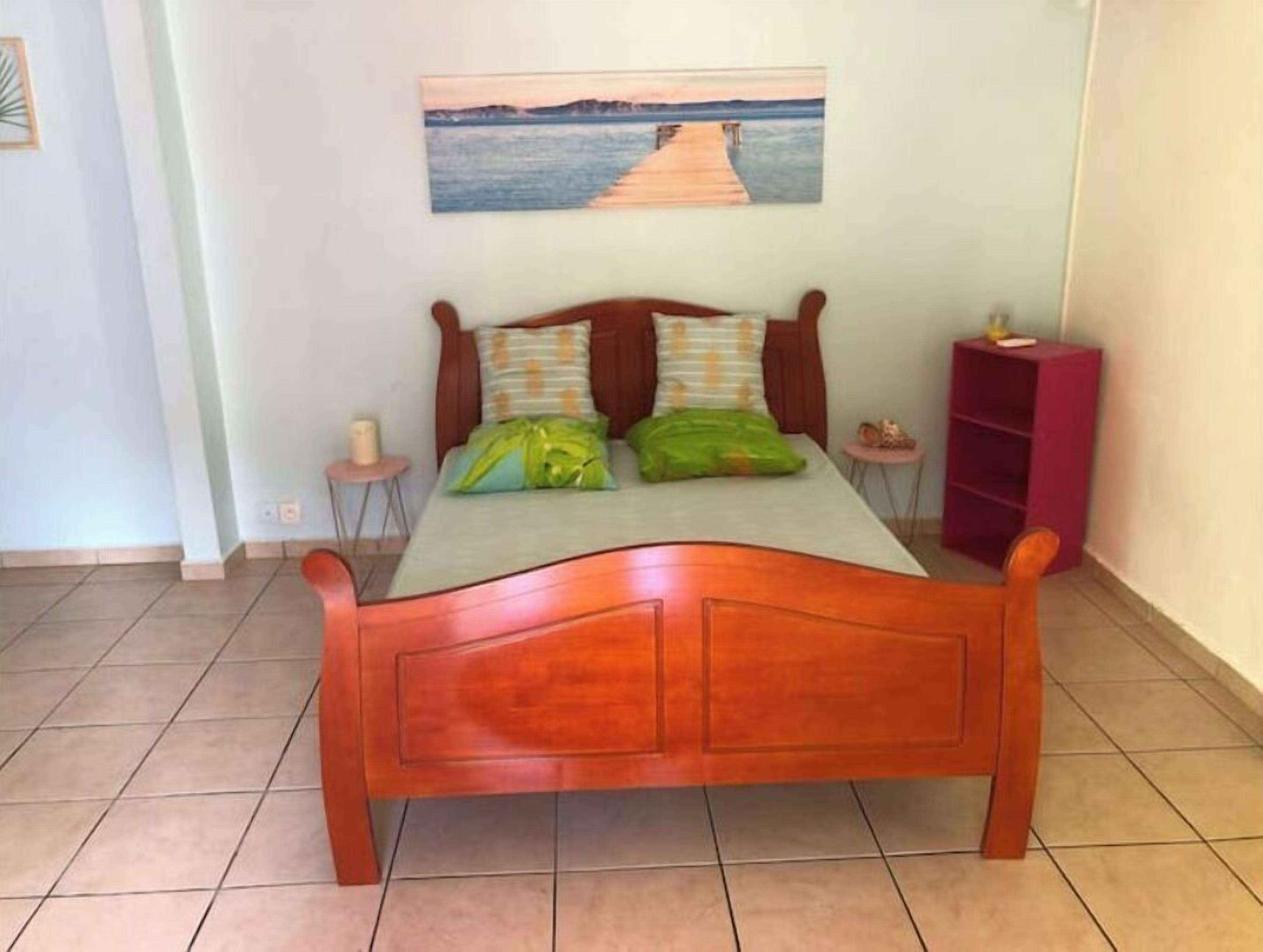 Un letto di legno con due cuscini, un comodino, una mensola rosa e un quadro di un molo sulla parete.