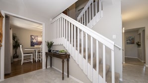 A staircase with white railings, a console table with a plant, and a 'welcome' sign.