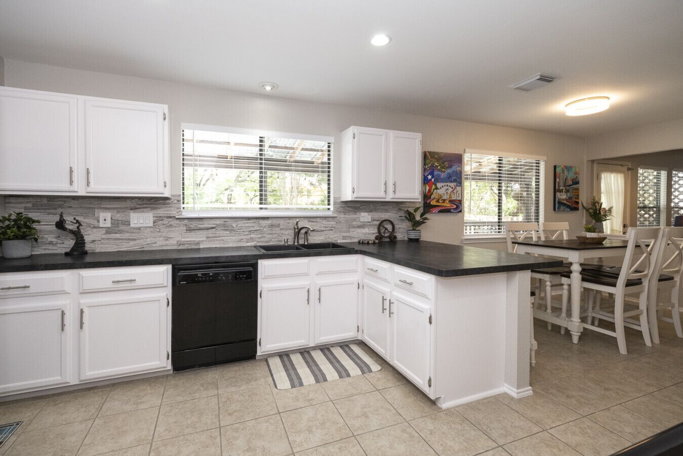 A kitchen with white cabinets, a dishwasher, a sink, and a dining area with chairs.