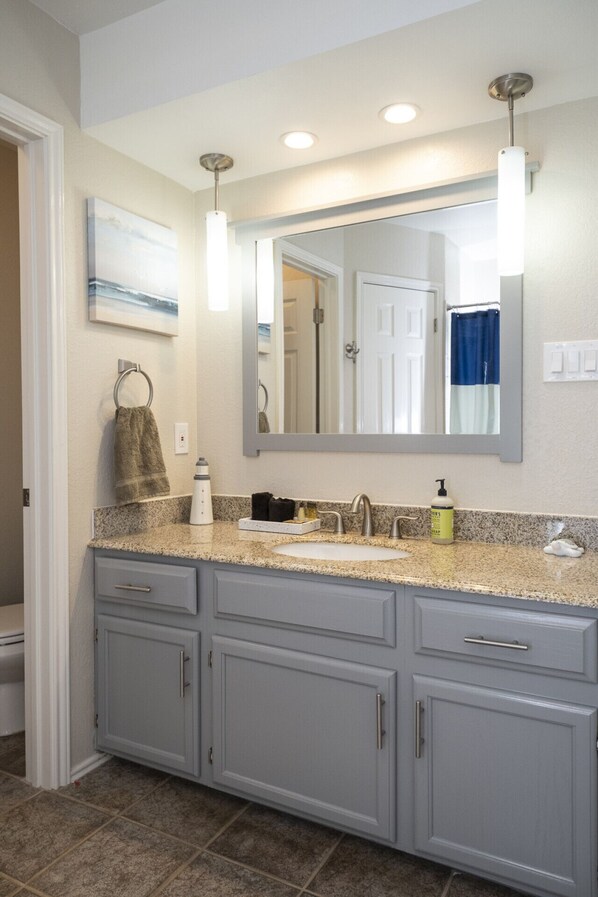 Une salle de bain avec un comptoir en granit, un lavabo, un miroir et un porte-serviettes.