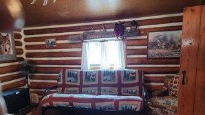 A log cabin interior with a sofa, a chair, a fan, and a rug. - Historic Ft Wilderness Cabin (South Fork)