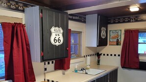 Une cuisine décorée avec des panneaux rappelant la Route 66, un coin repas avec une table et des chaises, et une fenêtre agrémentée de rideaux.