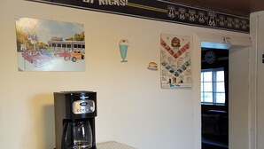 Un coin cuisine avec une machine à café posée sur un four à micro-ondes, une pancarte « Get Your Kicks! » au-dessus, et des objets de collection sur le thème de la Route 66 accrochés au mur.