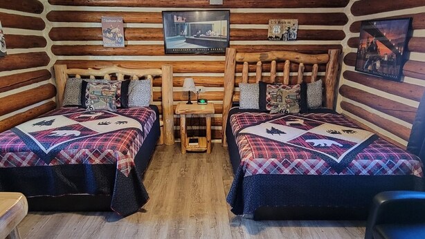 Une chambre aménagée dans un chalet en rondins, avec deux lits, une petite table et un luminaire fixé au plafond.
