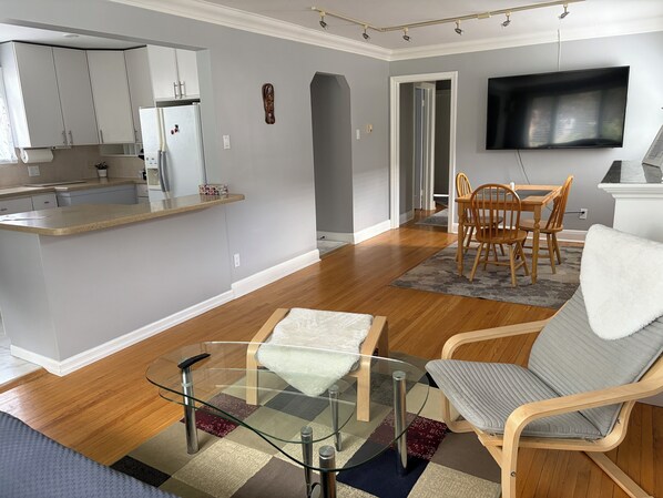 A modern living space with a kitchen, dining area, and a flat-screen TV mounted on the wall.