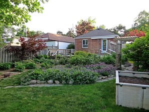 A residential property with a brick house, a wooden deck, and a well-maintained garden with various plants and flowers.