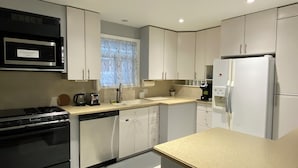 A modern kitchen with stainless steel appliances, white cabinetry, and a window with a floral curtain.