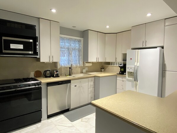 A modern kitchen with stainless steel appliances, white cabinetry, and a window with a floral curtain.
