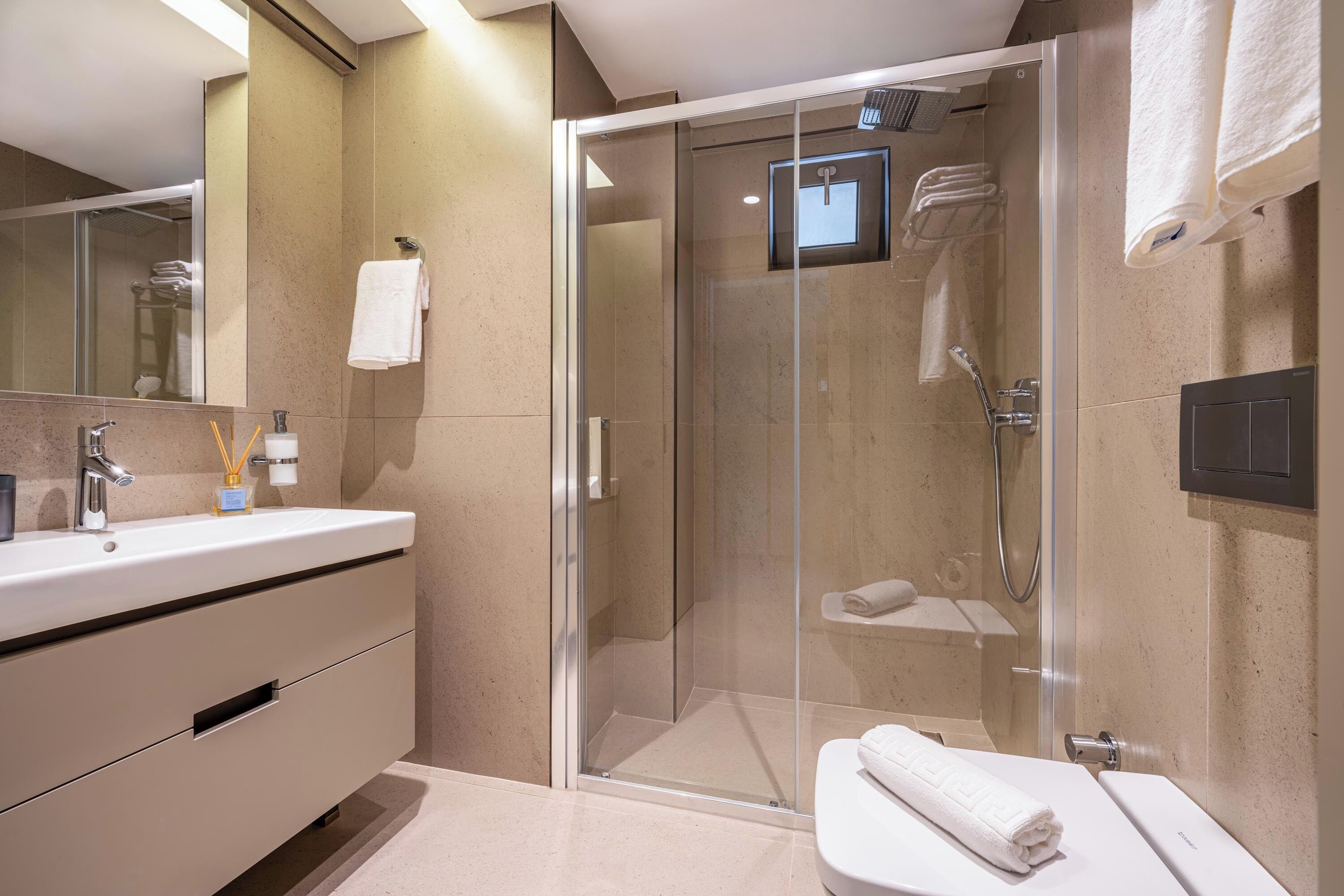 Une salle de bain moderne avec une douche à parois de verre, un meuble-lavabo avec un évier et un miroir, et des toilettes sur lesquelles est posée une serviette.