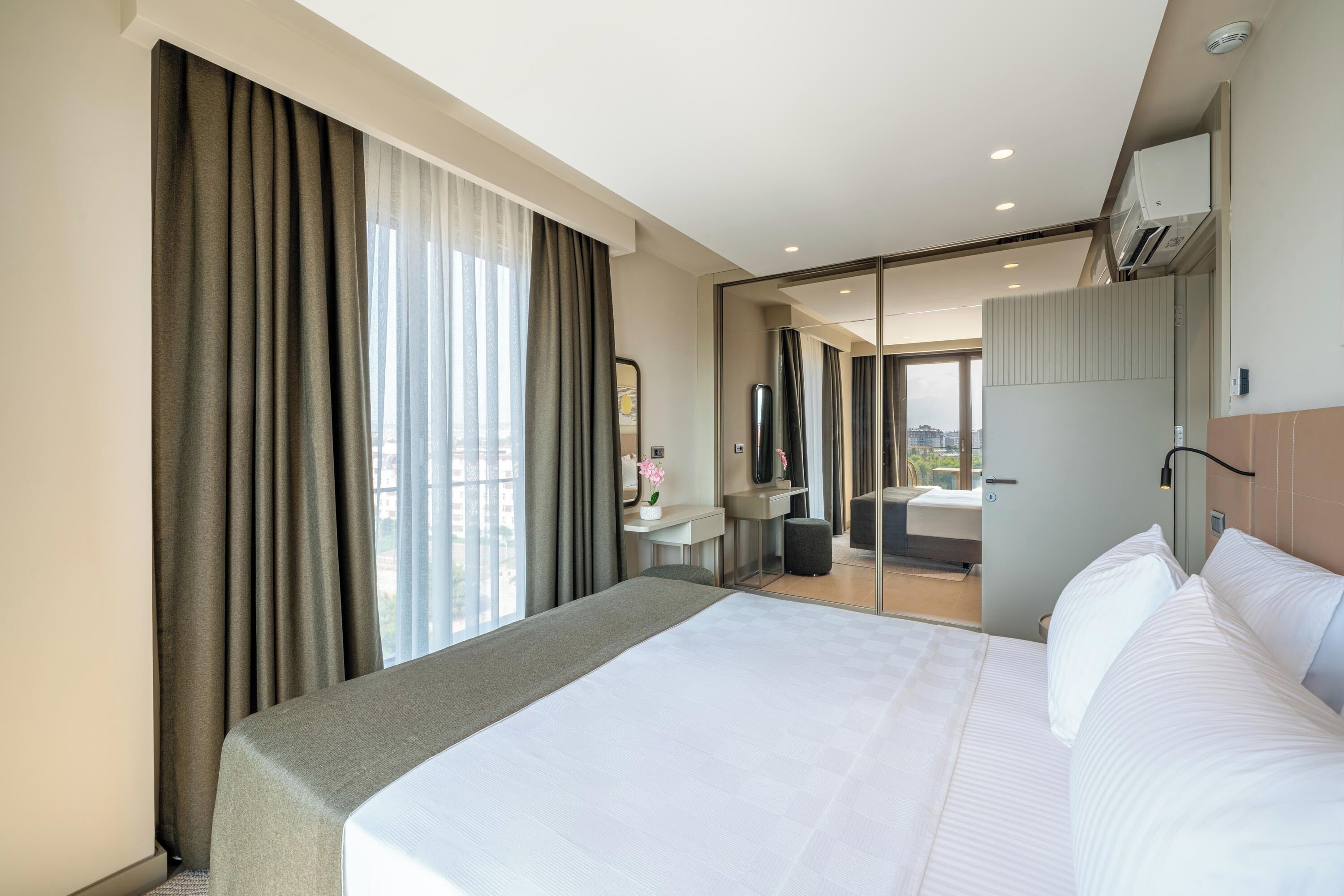 Habitación de hotel con una cama grande, un escritorio, un espejo y vistas a la ciudad.
