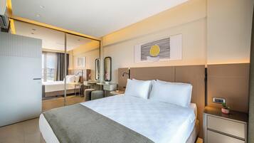A modern hotel room with a large bed, a desk, a chair, a mirror, and a small plant on the nightstand.